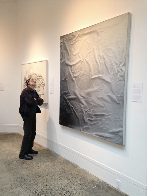 Carl stands next to an artwork that looks like a wrinkled sheet, examining it carefully