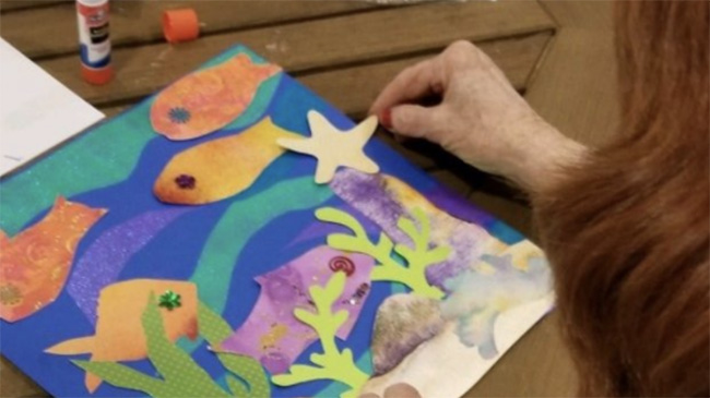 A woman works on a colorful cut paper artwork of fish