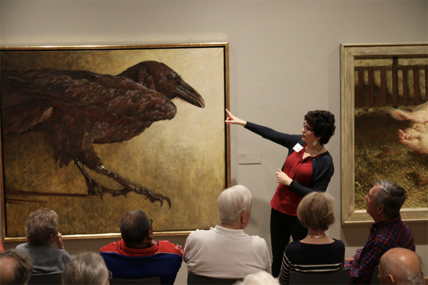 An ARTZ facilitator leading a group gestures at a painting of a crow