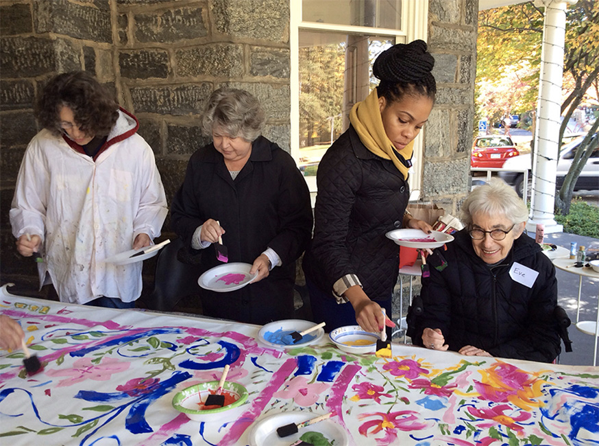 Eve, smiling brightly, works on a colorful painting of flowers with other ARTZ participants