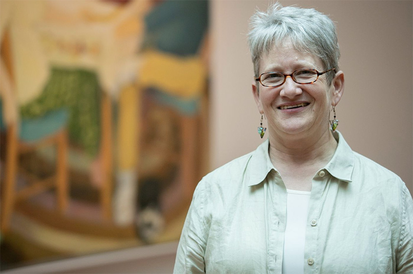 Portrait of Susan Shifrin in front of a painting smiling