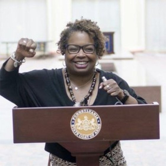 Community Liaison Toya triumphantly raises her fist at a podium