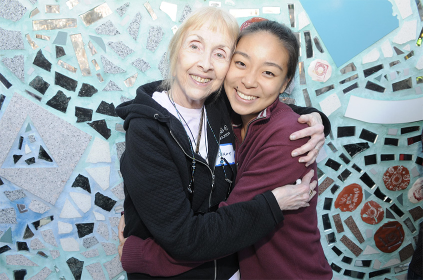 A Jefferson student and her ARTZ mentor embrace in front of a tile mural