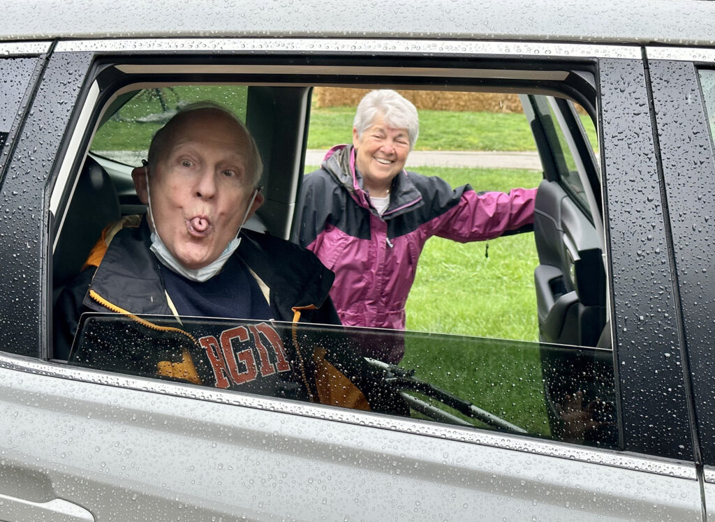 Don Kahn pictured through a car window sticking his tongue out with Jackie Kahn in the background laughing