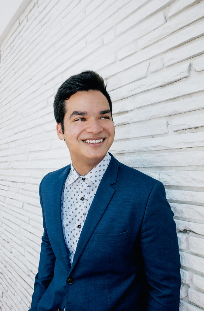 Ahmed smiling against a white brick wall